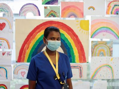 An NHS worker in a face mask with drawings of rainbows behind