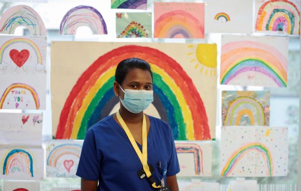 An NHS worker in a face mask with drawings of rainbows behind