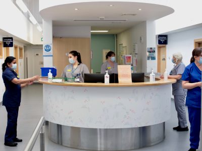 An NHS reception desk with staff in face masks