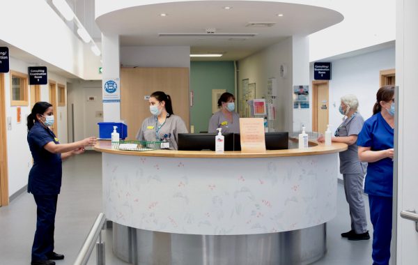 An NHS reception desk with staff in face masks