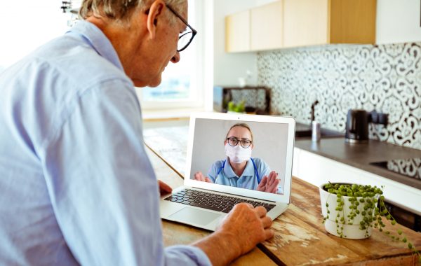An older man has a video call with a clinician who is wearing a mask