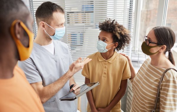 A doctor talks to a family including a teenage boy, all wearing masks