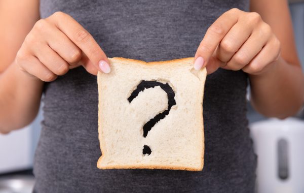 A woman holds a slice of bread with a question mark cut out of it