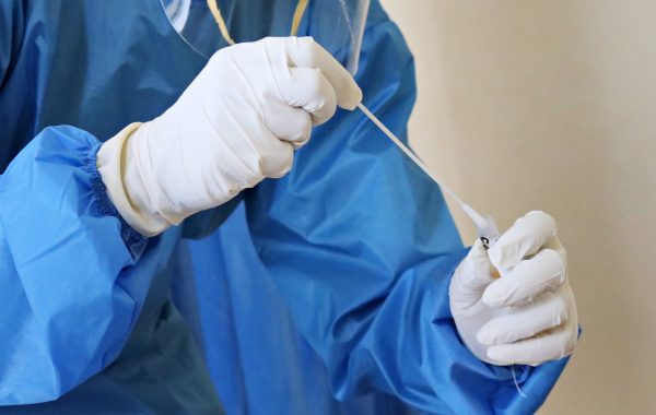 person in gown and latex gloves puts swab in sample tube.