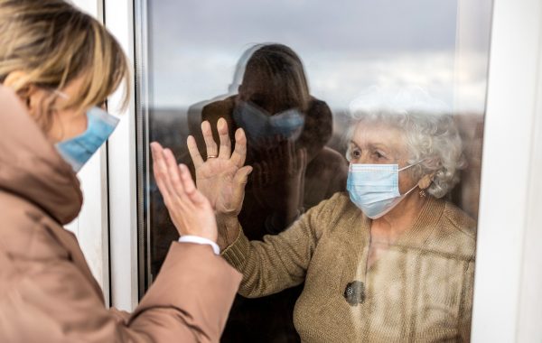An elderly woman in a care home looks through a window during a visit from her family during the COVID pandemic