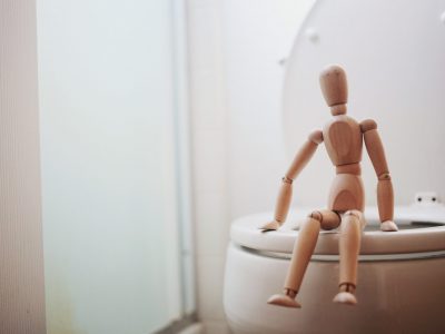 A wooden artist's model sitting on the edge of a toilet