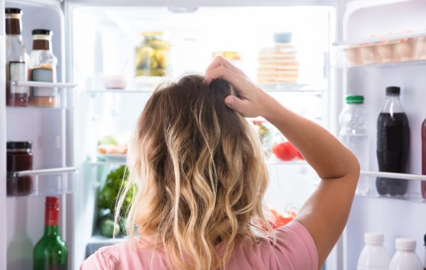 A woman scratches her head in confusion while looking in a fridge