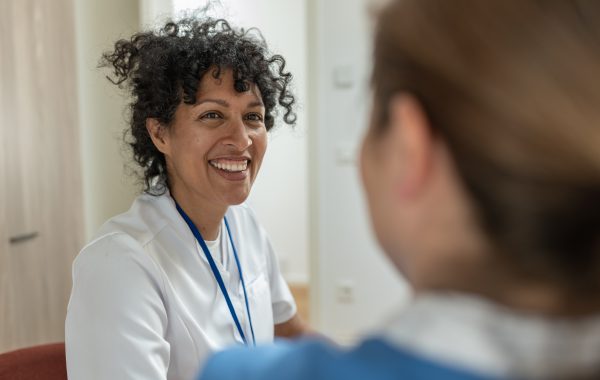 A smiling woman wearing a lanyard talking to another person