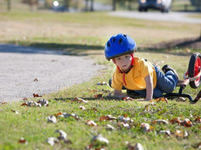 A toddler has fallen off their bike and is lying on some grass