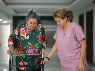 A nurse is assisting a senior adult patient walking down a hospital corridor