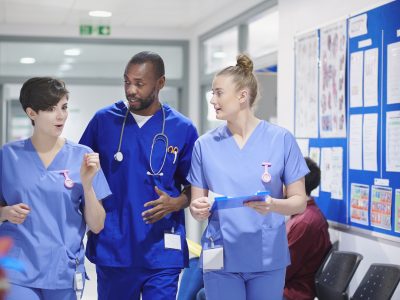Three healthcare professionals talking in a hospital corridor