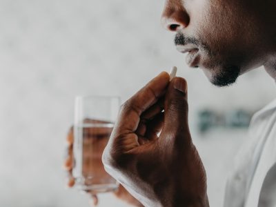 A man is holding a glass of water about to take a sip with his medication