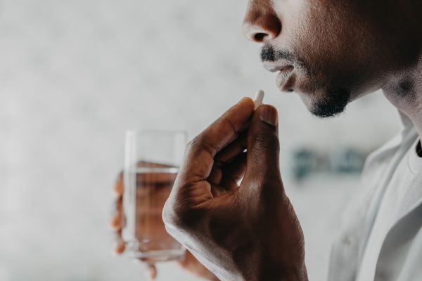 A man is holding a glass of water about to take a sip with his medication