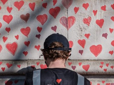 A person draws hearts on a Covid memorial wall