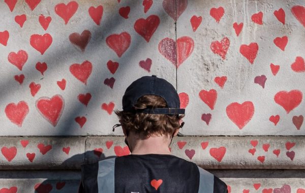 A person draws hearts on a Covid memorial wall