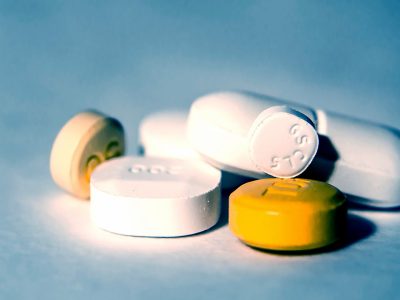 Pills of different shapes, sizes and colours are laid out on a blue surface