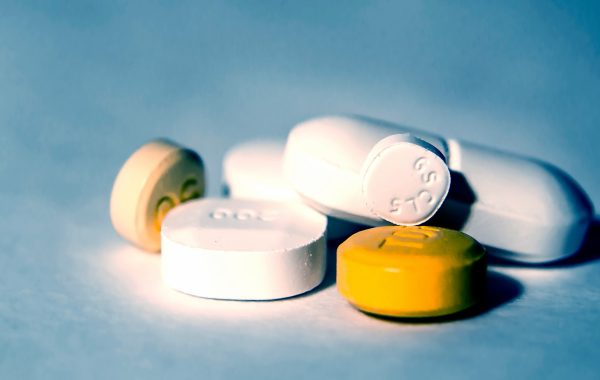 Pills of different shapes, sizes and colours are laid out on a blue surface