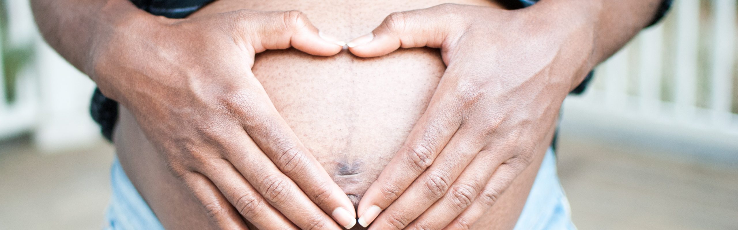 A pregnant woman holds her hands in a love heart shape over her belly