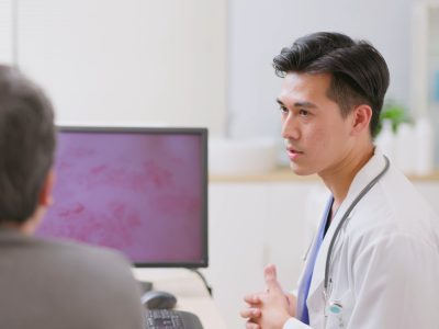 A doctor talks to a patient with shingles rash on a screen between them