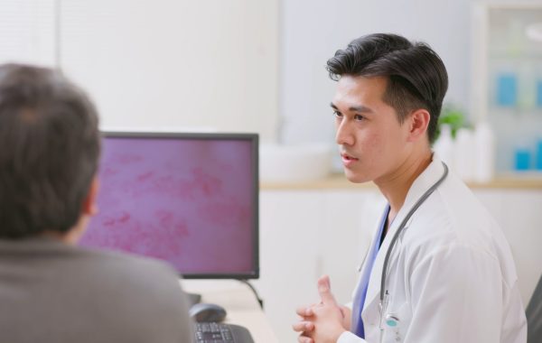 A doctor talks to a patient with shingles rash on a screen between them