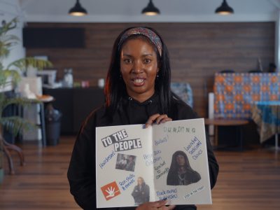 Screenshot from the video, with a participant holding up her zine to the camera