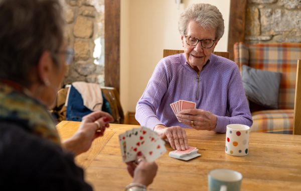Two senior women playing cards and drinking tea